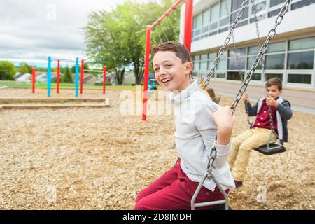 Die Jungen auf dem Spielplatz schaukeln am Schultag Stockfoto