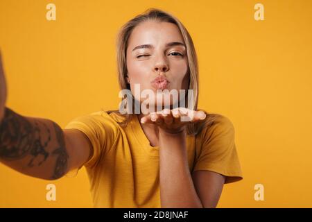 Bild von jungen freudigen Frau bläst Luft Kuss und nehmen Selfie-Foto auf gelbem Hintergrund isoliert Stockfoto