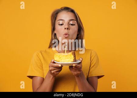 Bild der kaukasischen freudigen Frau, die am Geburtstag Kerze ausbläst Kuchen isoliert auf gelbem Hintergrund Stockfoto