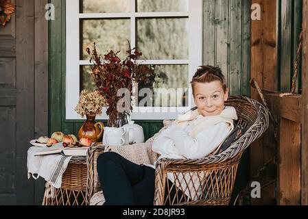 Ein Junge im Sessel, der sich auf der Veranda amüsieren kann Der Hinterhof mit Herbstdekorationen Stockfoto