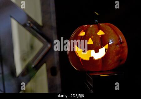 Gelsenkirchen, Deutschland. Oktober 2020. Ein dekorativer Kürbis mit Gesicht leuchtet vor einer geschlossenen Haustür. Aufgrund der zunehmenden Anzahl von Corona-Infektionen werden viele Türen dieses Jahr an Halloween geschlossen bleiben. Quelle: Caroline Seidel/dpa/Alamy Live News Stockfoto