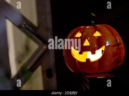 Gelsenkirchen, Deutschland. Oktober 2020. Ein dekorativer Kürbis mit Gesicht leuchtet vor einer geschlossenen Haustür. Aufgrund der zunehmenden Anzahl von Corona-Infektionen werden viele Türen dieses Jahr an Halloween geschlossen bleiben. Quelle: Caroline Seidel/dpa/Alamy Live News Stockfoto