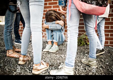 Traurige Einschüchterung Moment. Mädchen sitzen auf dem Boden Mobbing in Schulhof Stockfoto