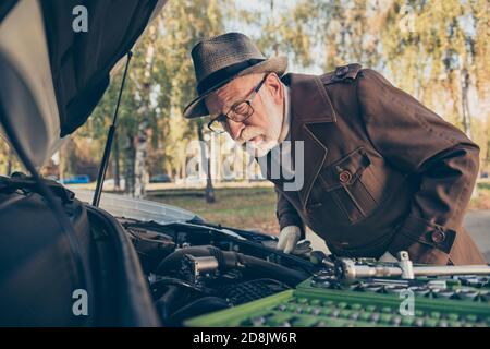Foto von pensionierten alten Mann aussehen Motor Untersuchung Problem Automobil Befestigung Tragen Sie braune Mantel Kappe Augenbrille außen Stockfoto