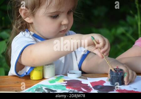 Ein Mädchen von 2 3 Jahren sitzt an einem Tisch und zeichnet mit bunten Farben. Kreativität der Kinder. Hobbys für Kinder. Stockfoto