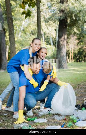 Glückliche Familie umarmt Vater beim Sammeln von Plastikmüll im Wald, Ökologie Konzept Stockfoto