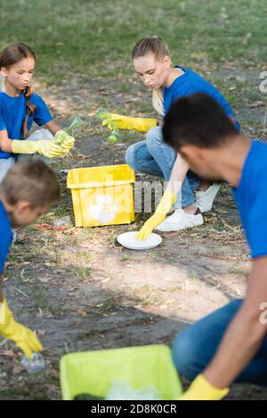 Mutter und Tochter sammeln Plastikflaschen in Müllcontainern bei Vater und Sohn auf verschwommenem Vordergrund, Ökologie-Konzept Stockfoto