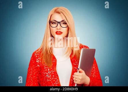 Eine schöne junge Frau in Brillen stehen mit einem Laptop in der Hand trägt rote Spitzenjacke, weißes formelles Hemd isoliert auf blauem Hintergrund mit Stockfoto