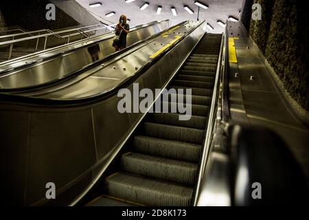 W Woman schaut auf ihr Handy auf einer Rolltreppe in der U-Bahn-Station Pie IX in Hochelaga, Montreal, QC, Kanada Stockfoto