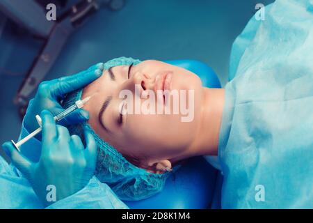 Inhalt Attraktive Modell Augen geschlossen mit Botulinumtoxin Hyaluronsäure Injektion auf die Stirn in einem Klinik-OP-Raum; O.R Hintergrund. Schöner Stockfoto