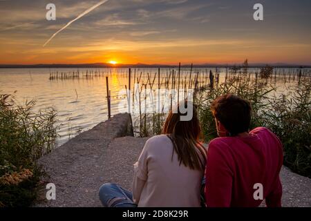 Liebeskonzept. Nicht identifiziertes Hochzeitspaar beobachtet den Sonnenuntergang, der neben dem 'La Albufera' See in Valencia, Spanien, sitzt. Stockfoto