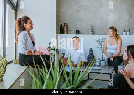 Wellness-Coach, der mit einer Gruppe junger Menschen arbeitet. Junge Frau im Gespräch mit Menschen über Gesundheit im Wellness-Center oder Yoga-Studio. Stockfoto