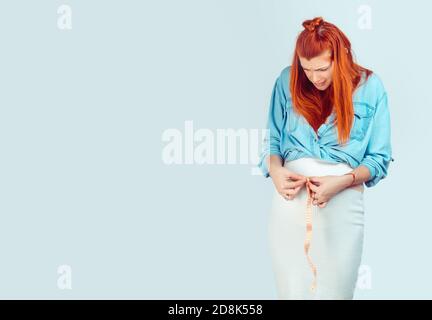 Lustige junge Frau in casual Outfit Messung Taille schwanger und Blick erschrocken auf Bauch isoliert auf hellblau. Unglücklich, indem man Fett während Stockfoto