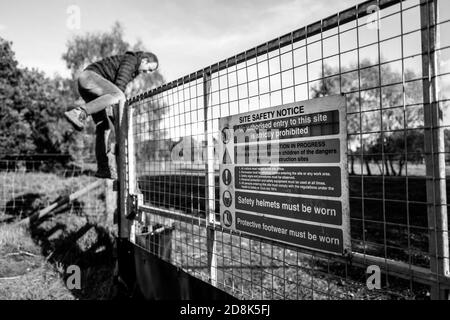 Erwachsener Mann klettert Zaun in eine kontaminierte Heide, die für militärische Ausbildung verwendet wird. Stockfoto