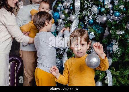 Glückliche Familie - Vater, Mutter und Söhne alle zusammen schmücken den Weihnachtsbaum im Wohnzimmer. Familie mit Kindern feiern Winterferien. Stockfoto