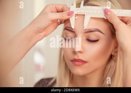 Ändern der Brauenform. Stylist Messung der Augenbrauen mit dem Lineal. Mikropigmentierung Arbeit Flow in einem Schönheitssalon. Frau mit ihrem Auge br Stockfoto