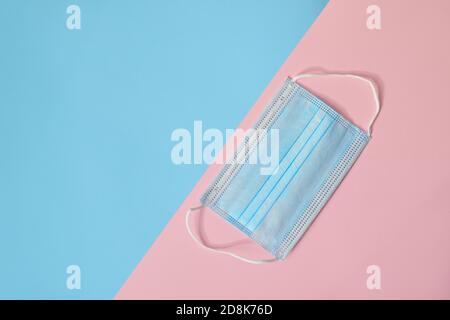 Medizinische Einweg-Schutzmaske auf einem rosa und blauen Hintergrund. Das Konzept des Schutzes der Gesundheit vor dem Virus. Platz kopieren, Draufsicht. Stockfoto