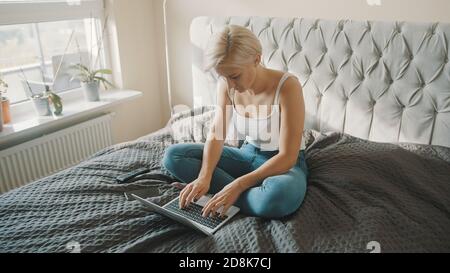 Junge kaukasische Frau mit Laptop in ihrem Schlafzimmer. Freiberufliche Mitarbeiterin, die bequem von zu Hause aus arbeitet. . Hochwertige Fotos Stockfoto