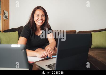 Lächelnde Geschäftsfrau mit mittlerem Erwachsenenalter, die von zu Hause aus mit einem Laptop arbeitet Während der Sperre Stockfoto