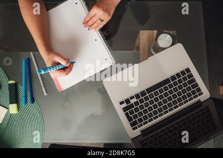 Direkt über Schuss der Geschäftsfrau, die notwendige Notizen in Notepad Während der Vorbereitung auf wichtige Treffen zu Hause Stockfoto