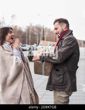 Mann, der seiner Freundin ein großes weihnachtsgeschenk gibt. Emotional überrascht glücklich Mädchen erhält ein Geschenk draußen. 8. März, Neujahrsüberraschung. Stockfoto