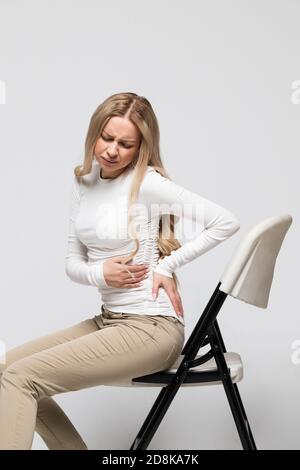 Frau mit Schmerzen, Muskel- oder chronischen Nervenschmerzen im Rücken, sitzend auf einem Stuhl. Erkrankungen des Bewegungsapparates, der Wirbelsäule, Skoliose, Osteoporose Stockfoto