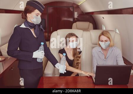 Flugbegleiter in Gesichtsmaske als Schutz vor covid-19 dient Passagiere im Business Jet. Stockfoto