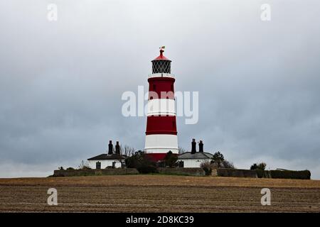 Der rot-weiß gestreifte Happisburgh Leuchtturm an der Norfolk Küste, England. Der Leuchtturm steht an einem bewölkten Tag in einem schlammigen Feld. Stockfoto