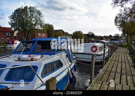 Kleine Vergnügungsboote und Yachten werden an einer hölzernen Promenade entlang des Flusses Waveney in der Stadt Beccles in Suffolk, England, gebunden. Stockfoto