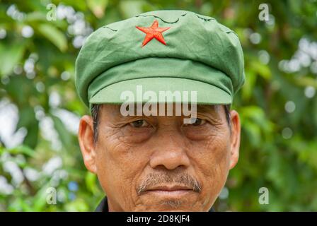 Phitsanulok, Thailand - 26. AUGUST 2017: Der ältere Mann des Hmong-Stammes trägt eine Mütze im Mao-Stil und steht im grünen Wald vor verschwommenem Hintergrund. Phitsanulok. Stockfoto