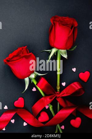 Schöner Valentinstag Hintergrund mit roten Rosen und Herzen auf schwarzem Hintergrund. Flach liegend, Kopierbereich Stockfoto