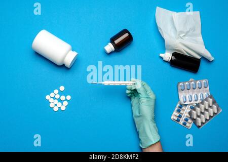 Arzt in Latexhandschuhen hält Quecksilberthermometer über blauem Hintergrund Mit Pillen Stockfoto