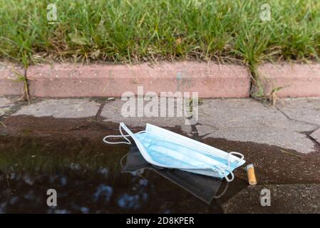 Schützende medizinische Gesichtsmaske auf einer Stadtstraße verloren. Die blaue Maske liegt in der Nähe der Pfütze. Stockfoto