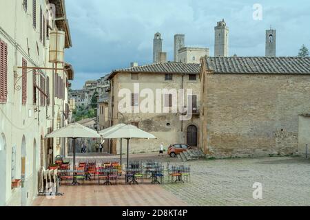 SAN GIMIGNANO, ITALIEN - september 20 2020: Stadtbild mit leeren Tables auf dem fast leeren sant Agostino Platz mit Türmen, die sich im Bacvkground abzeichnen, Schuss i Stockfoto