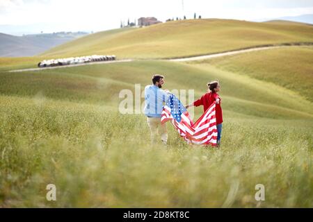 Ein verliebtes Paar, das an einem schönen sonnigen Tag die amerikanische Flagge auf einer Wiese hält. Wahl, Kampagne, Freiheitskonzept Stockfoto