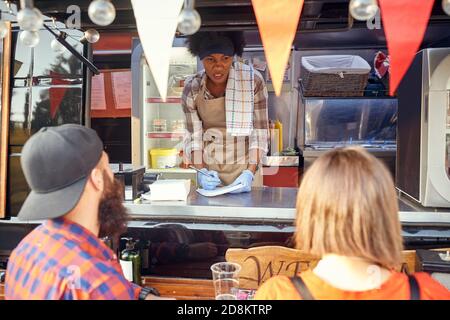 Junge afro-amerikanische Frau, die von einem Paar um Essen bestellt wird Der Kunden und schreiben sie auf Stockfoto