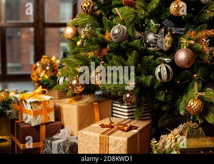 Weihnachtsbaum mit goldenen Kugeln verziert. Unter dem Weihnachtsbaum eine große Anzahl von Weihnachtsgeschenken. Weihnachtsfeiertagskonzept. Stockfoto