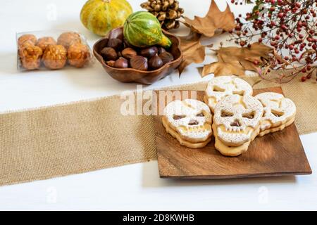 Süßer Möwenkeks auf dem Holzteller, Panelles de piñones, Kastanien und Kürbisse auf dem Tisch, vorbereitet für Halloween. Süßigkeiten backen und Halloween Stockfoto
