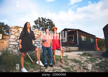 Drei Freunde, die Spaß haben und Schaufeln auf einer Ranch halten. Ranch Konzept Fotografie Stockfoto