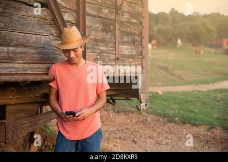 Junger Mann mit Cowboy-Hut, der den Sonnenuntergang vor einem hölzernen Vintage Train Wagon betrachtet. Ranch Konzept Fotografie Stockfoto