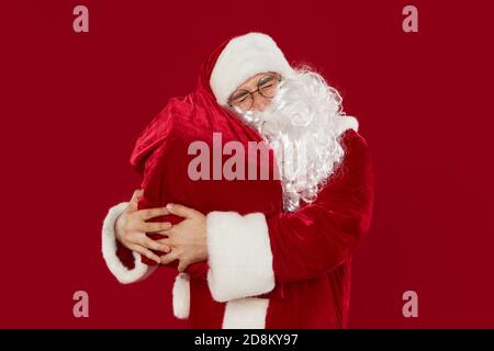 Glücklich zufrieden Weihnachtsmann hält volle Tasche mit Geschenken auf Ein roter Hintergrund Stockfoto