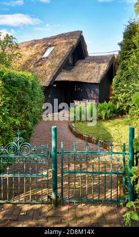 Haus mit einem alten Reetdach und einem hölzernen Sitzbereich hinter dem Gartenzaun mit einem metallenen Eingangstor. Stockfoto