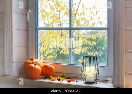 Orangefarbene Kürbisse auf Fensterbank, Kerzen, Herbstblätter, Laterne. Skandinavischer Stil. Stockfoto