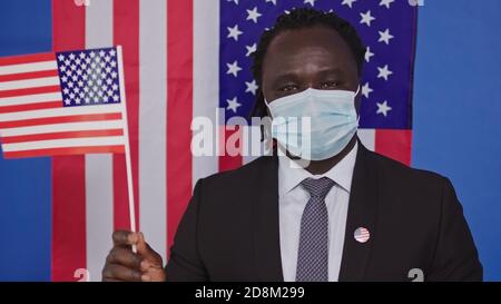 Afroamerikanischer Mann mit Gesichtsmaske Blick auf Kamera - US Flagge im Hintergrund . Hochwertige Fotos Stockfoto