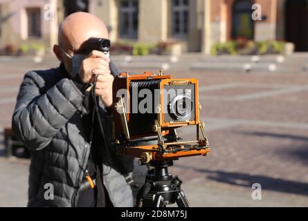 Krakau, Malopolska/Polen - 20.10.2020: Mann, der mit einer großformatigen Holzklappkamera im Vintage-Stil auf einem Stativ fotografiert. Aufnahme von Belichtungsdaten mit Stockfoto