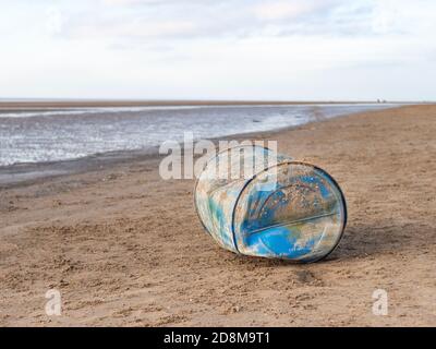 Ein abgeworfenes blaues Plastikfass, das an einem Sandstrand liegt Stockfoto