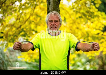 Ein Mann in den späten Sechzigern übt im Herbst mit einer Widerstandsband im Freien. Stockfoto