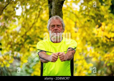 Ein Mann in den späten Sechzigern übt im Herbst mit einer Widerstandsband im Freien. Stockfoto