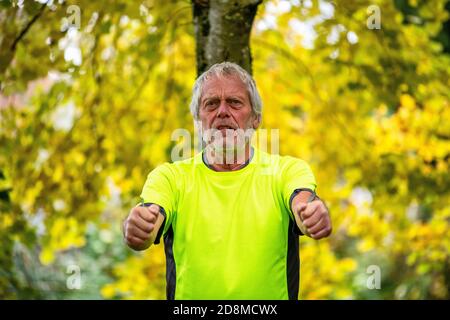 Ein Mann in den späten Sechzigern übt im Herbst mit einer Widerstandsband im Freien. Stockfoto