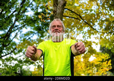 Ein Mann in den späten Sechzigern übt im Herbst mit einer Widerstandsband im Freien. Stockfoto